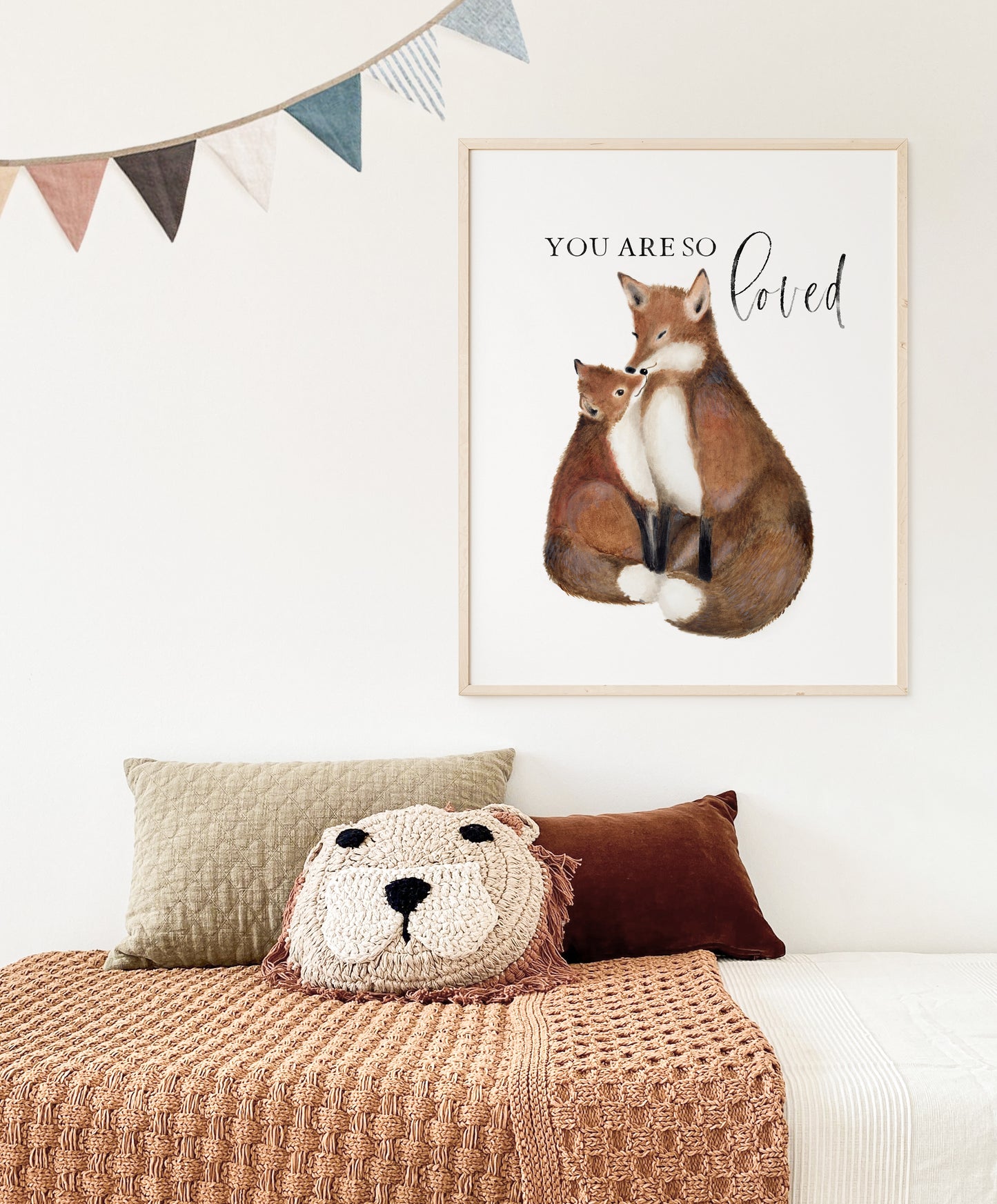 Artwork painting of a mother and baby fox with the words You are So Loved. The artwork is on a plain white background and is framed in a light wood frame. The picture hangs on a light colored wall over a child's bed. Art by Studio Q - Art by Nicky Quartermaine Scott