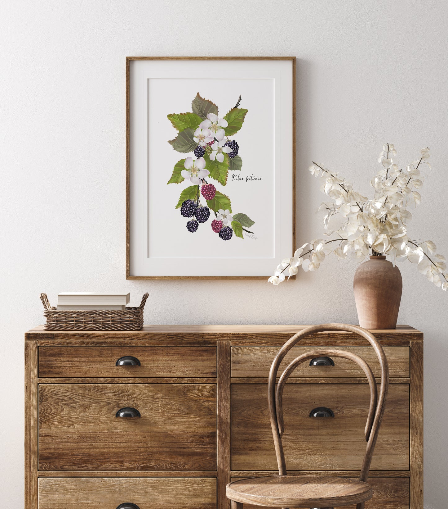 Wooden dresser with a framed blackberries and botanical print and vase of flowers on a light gray wall.