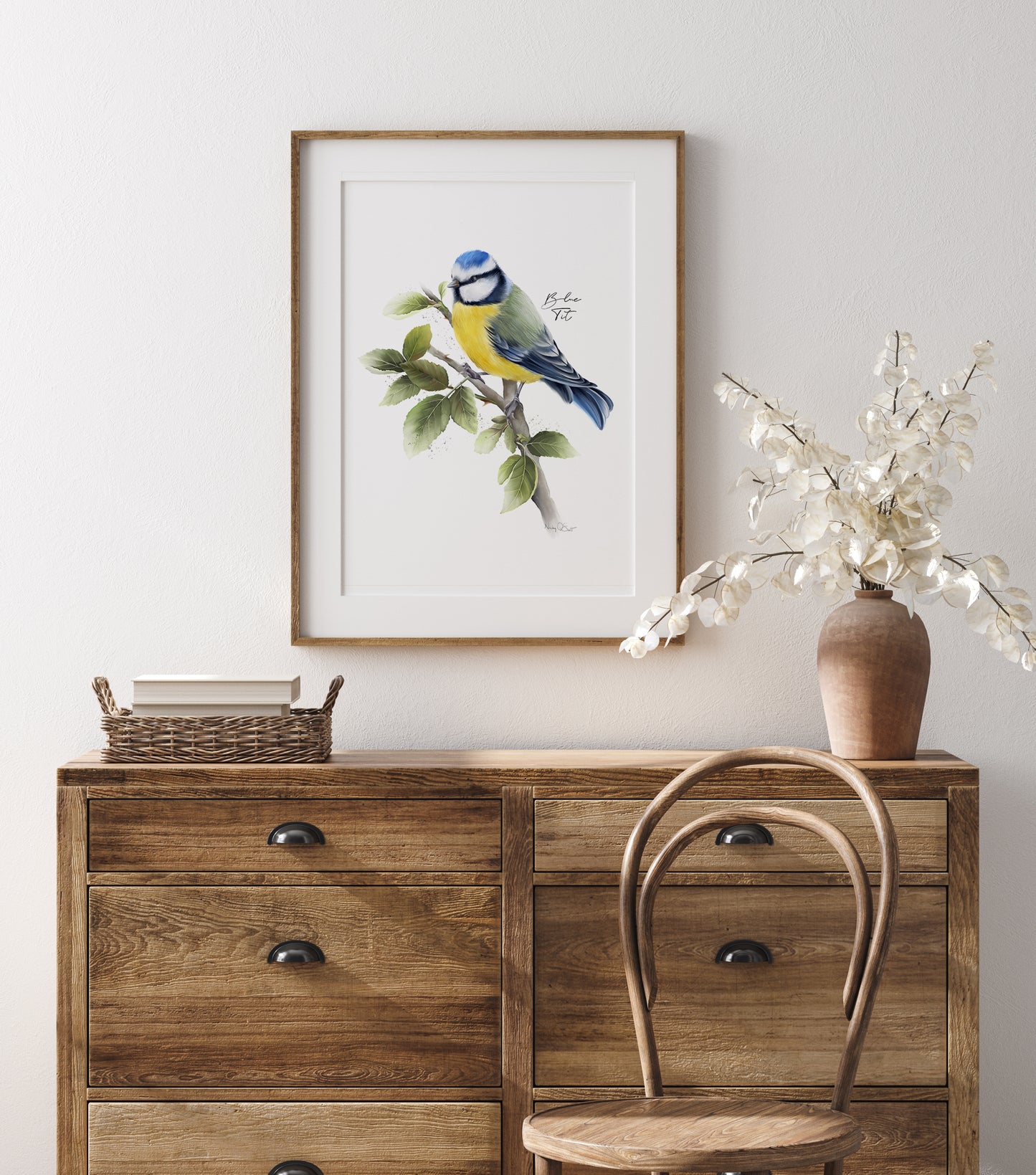 Wooden dresser with a framed blue tit bird print and vase of flowers on a white wall